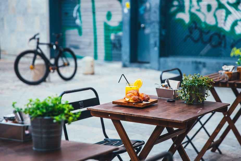 Outdoor café scene with wooden tables, a bicycle, and a vibrant mural.