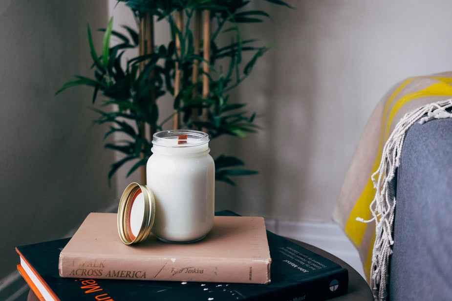 A cozy setting with a white candle on stacked books beside a plant.
