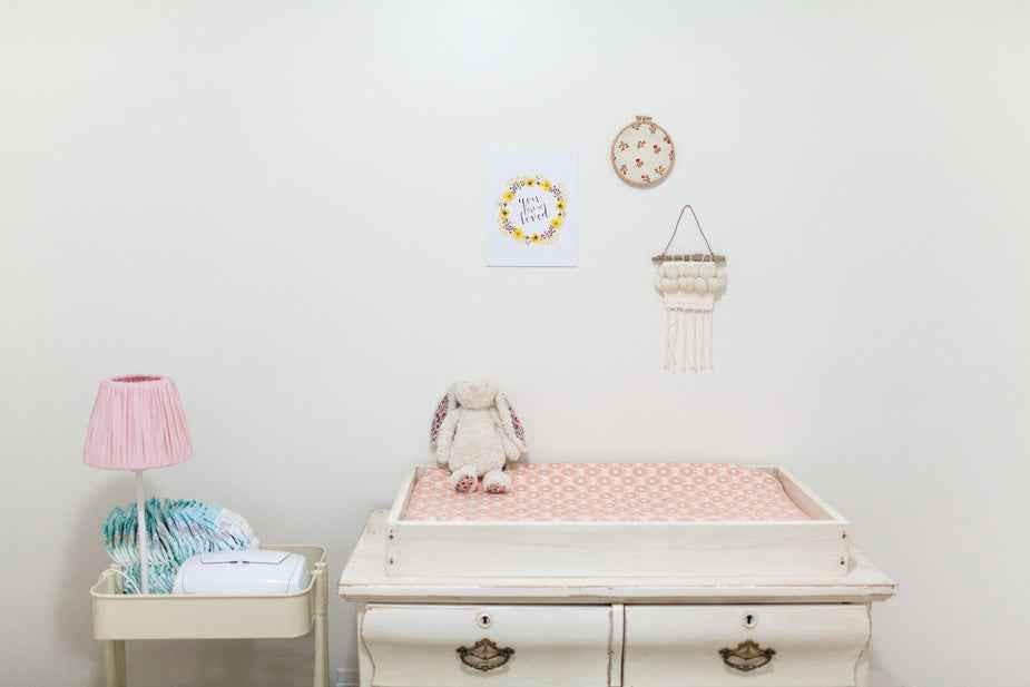A cozy nursery with a changing table, soft pink lamp, and decorative wall hanging.