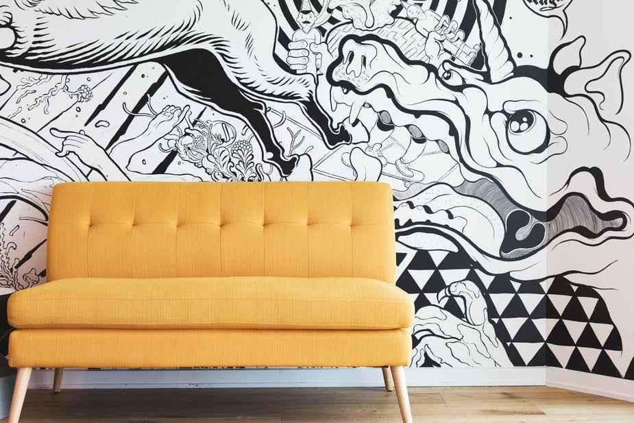 A yellow couch in front of a black and white mural featuring abstract designs and creatures.